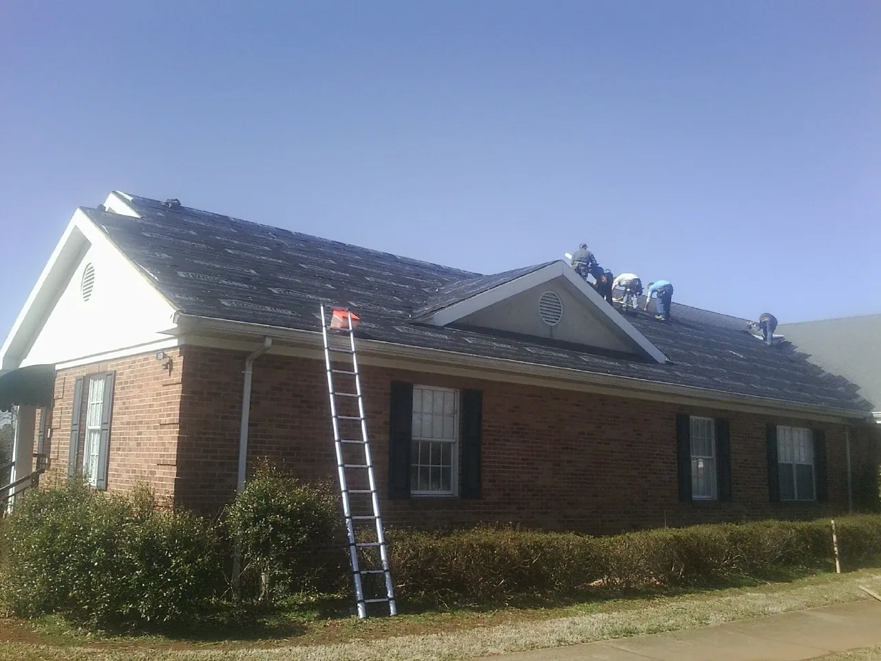 Crew tearing shingles off a brick ranch roof with a ladder set — Emergency Roof Repair work by our crew in Mosier