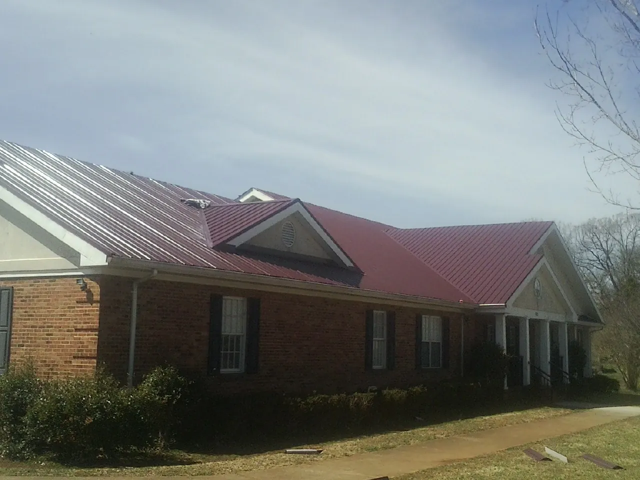 Red metal roof with gabled entries on a long brick building, from a Hail Damage Roof Repair job in Mosier